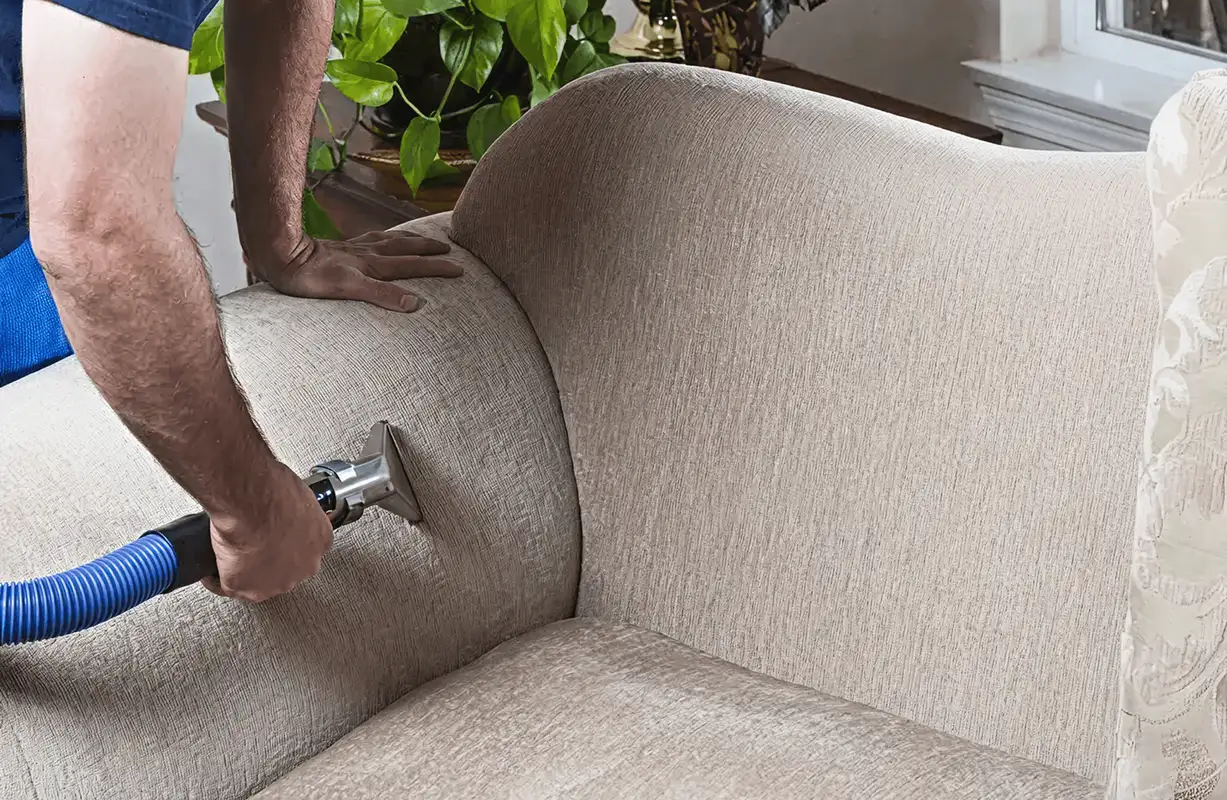 Professional upholstery cleaner deep-cleaning a fabric sofa with a handheld extraction tool and hose, Spokane, WA.
